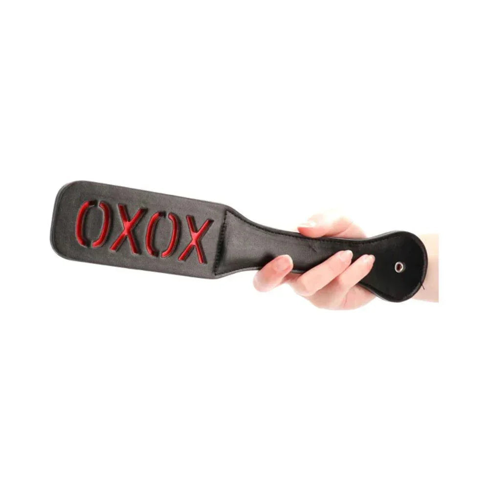 Black leather Ouch! 'XOXO' paddle with red stitched reversed lettering held by a hand