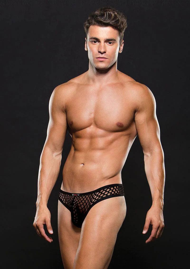 Muscular male model wearing black Envy Modern Fishnet Thong underwear against a dark background