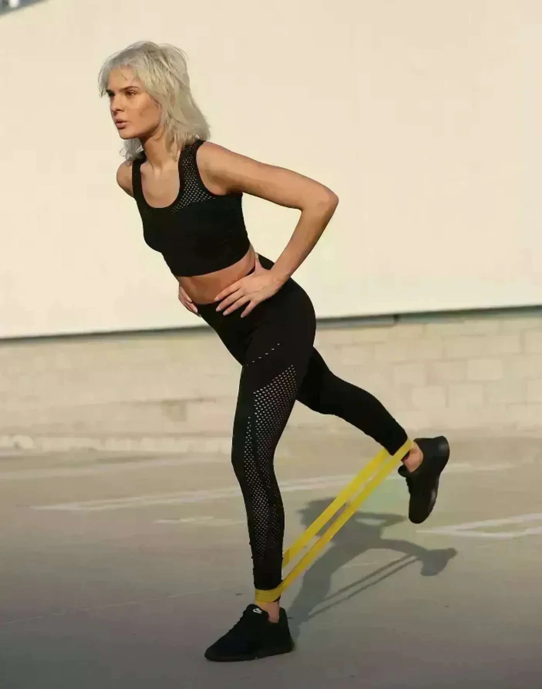 Woman exercising outdoors using yellow resistance body band on legs for workout