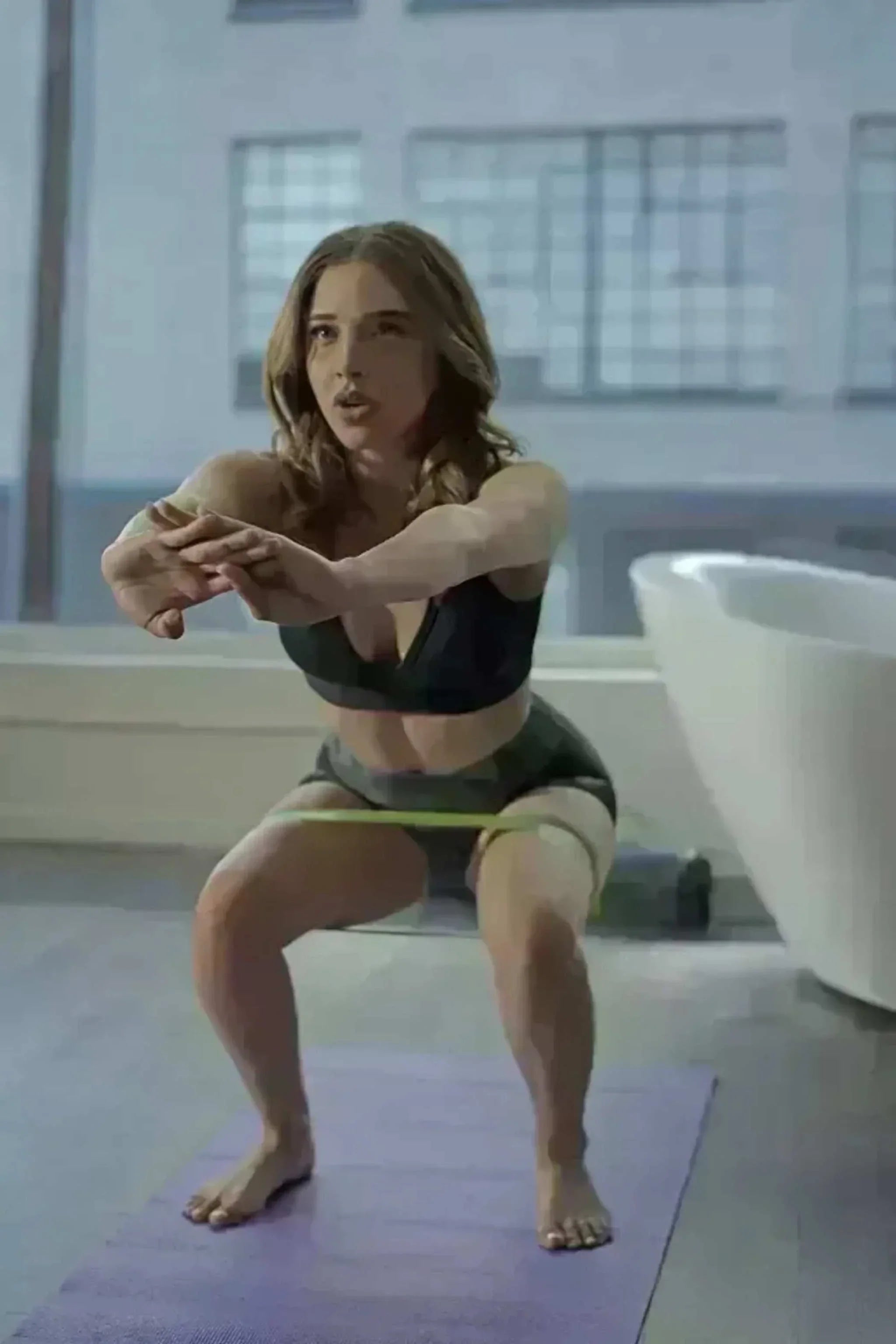 Woman exercising with resistance body bands on thighs doing squats indoors on purple yoga mat