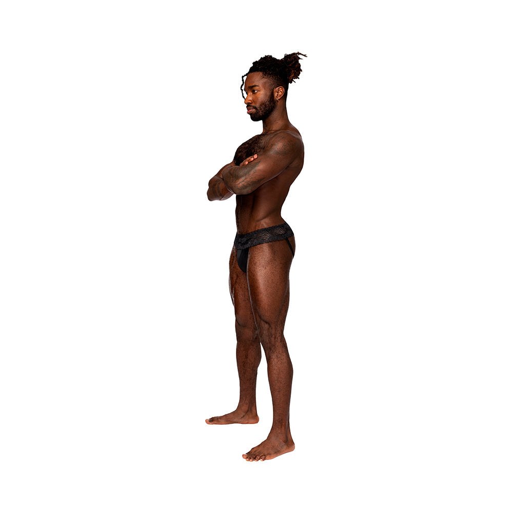 Male model wearing Male Power Sassy Lace Skirt Jock in black, size L/XL, showcasing sheer lace skirted waistband and stretch mesh pouch design.