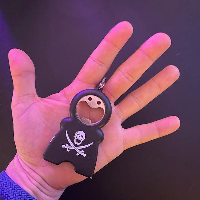TIM 4-in-1 Keychain with bottle opener, flashlight, and tape measure held in hand, pirate design on black compact tool