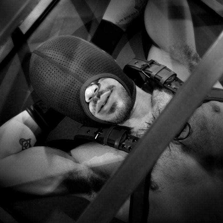Man wearing Fort Troff Black Ops Hood with perforated neoprene and large mouth opening, lying down in harness straps.