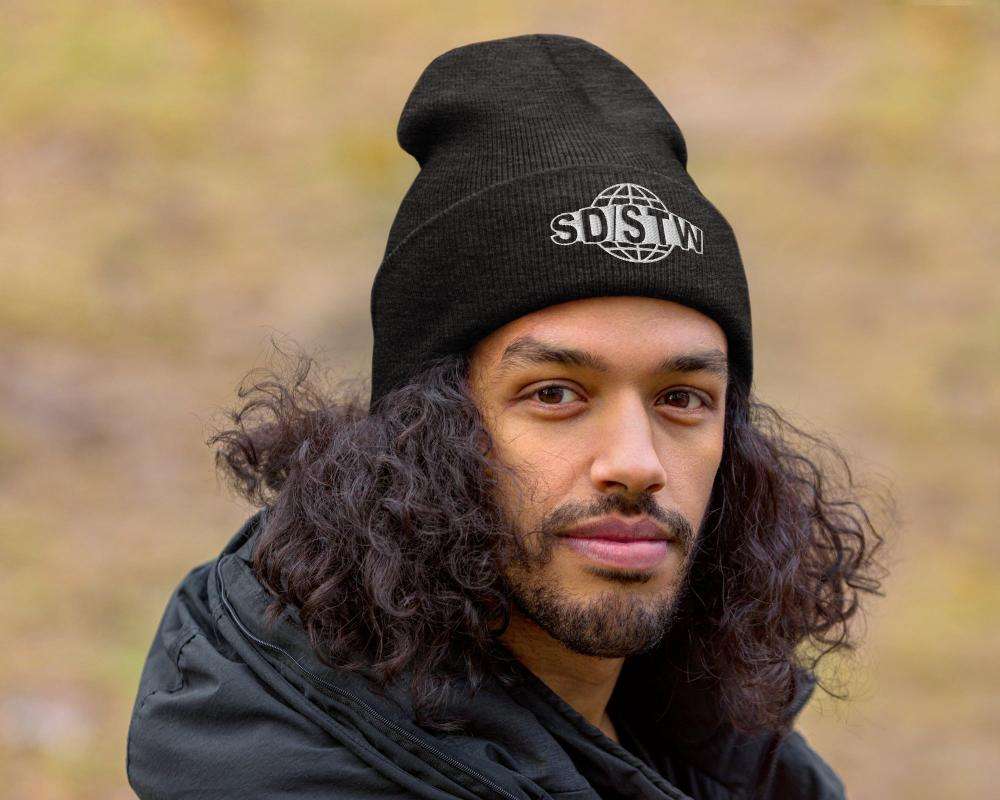 Man wearing black Suck Dick Save the World beanie with SD/STW logo outdoors