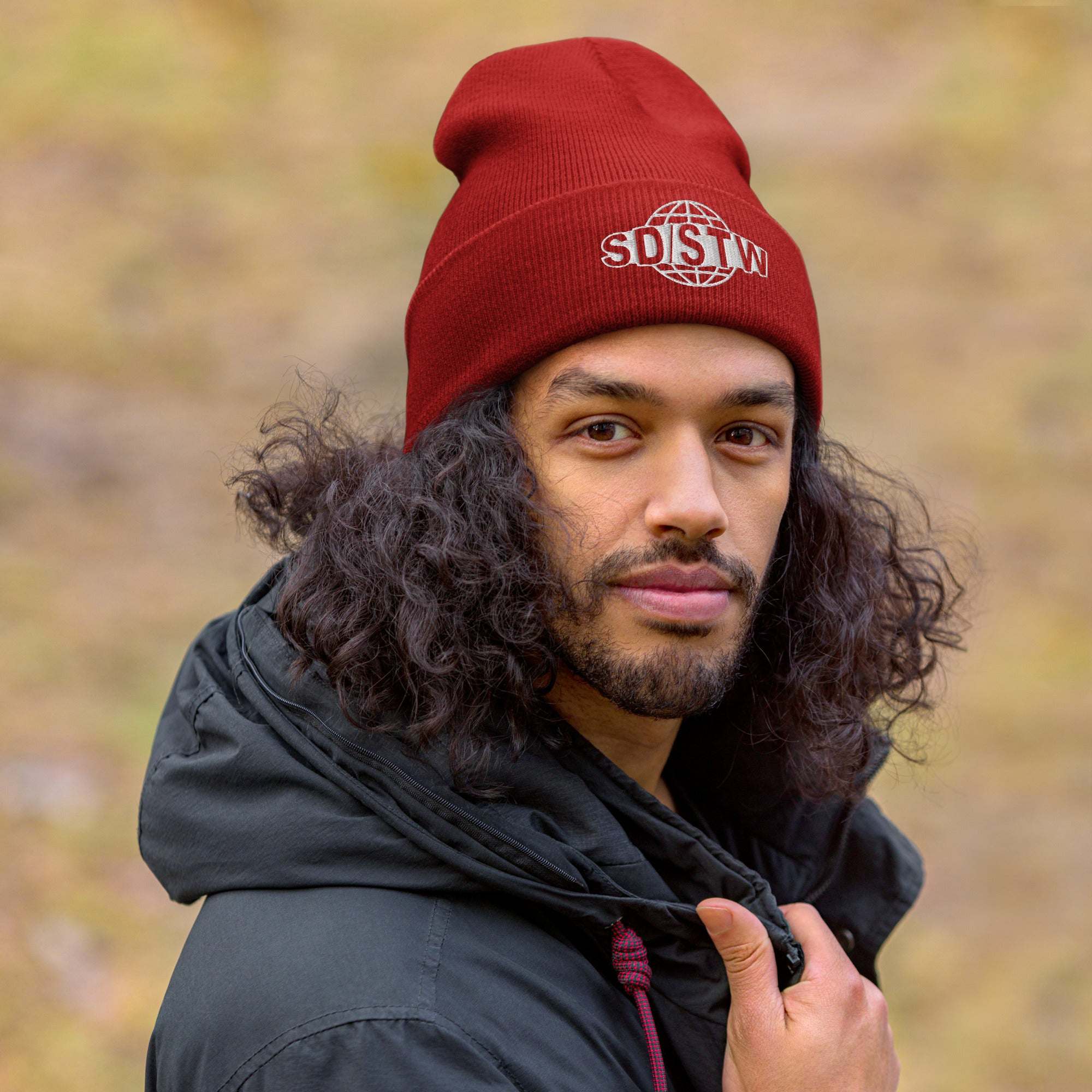 Red "Suck Dick Save The World (SD/STW)" beanie worn by a person outdoors in a chilly setting.