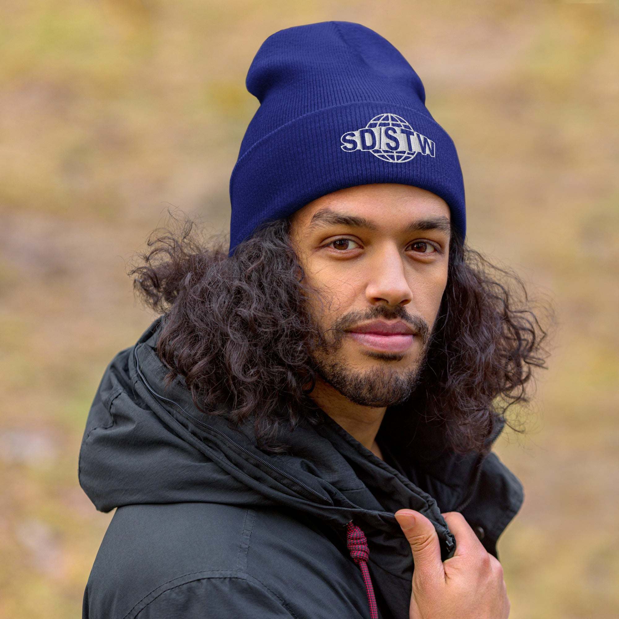 Man wearing navy blue Suck Dick Save the World beanie outdoors with curly hair and black jacket