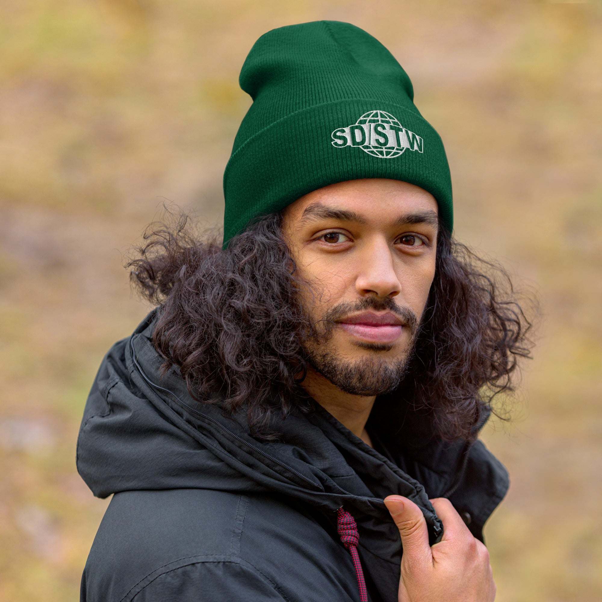 Man wearing green Suck Dick Save the World beanie with SD/STW logo outdoors