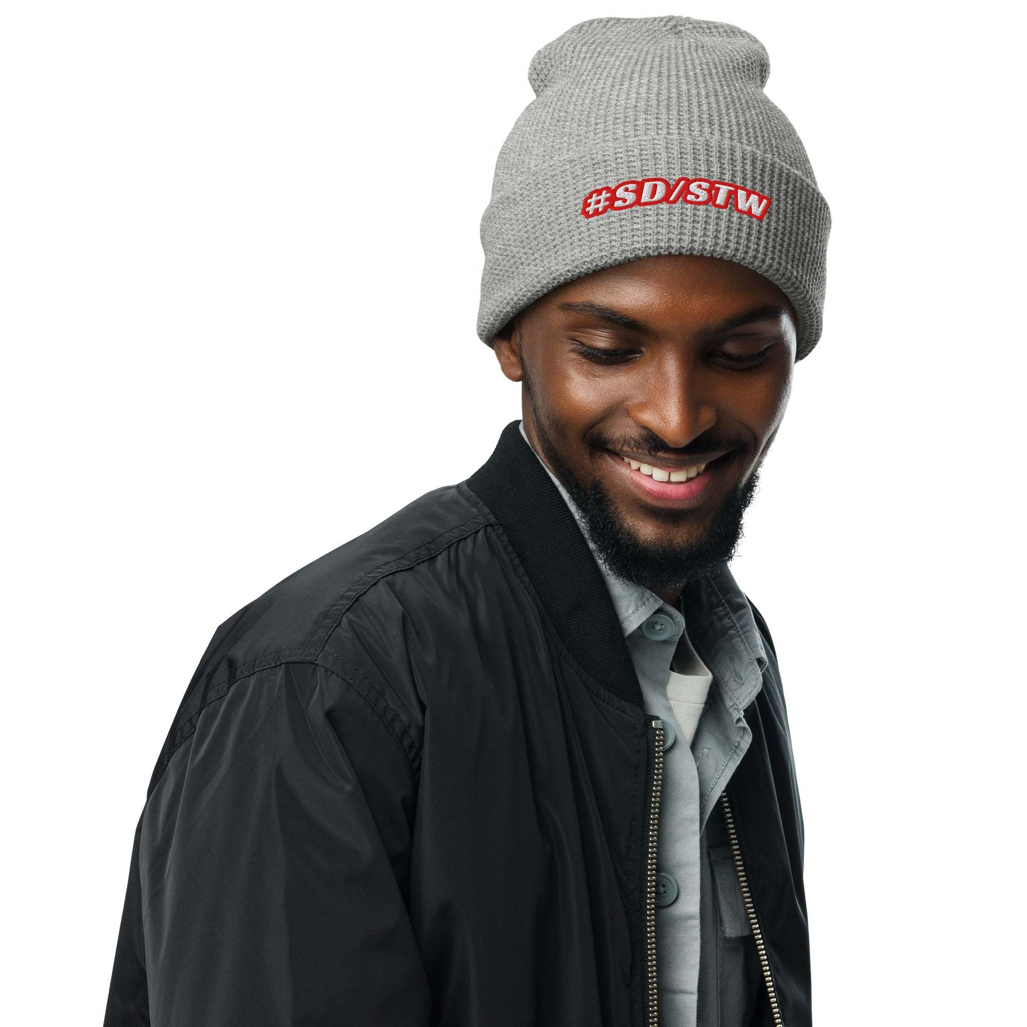 man wearing grey #SD/STW waffle beanie with red logo and black jacket smiling