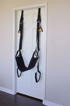 Black Door Jam Sex Sling with padded seat and adjustable straps hanging on a white door
