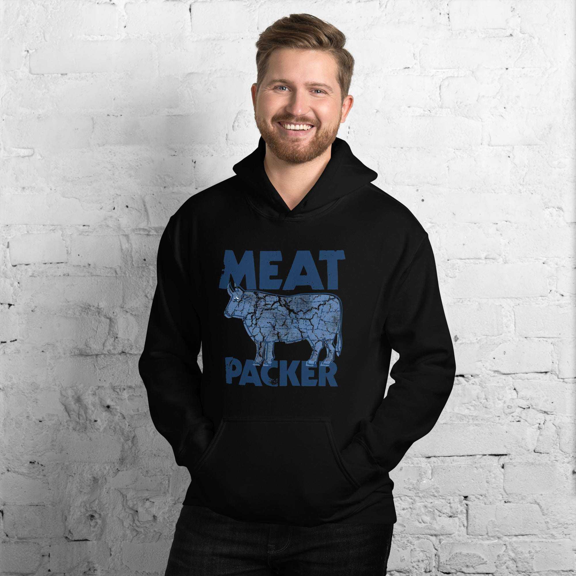 Man wearing black Meat Packer Pullover Hoodie with blue graphic text and cow illustration against white brick wall background