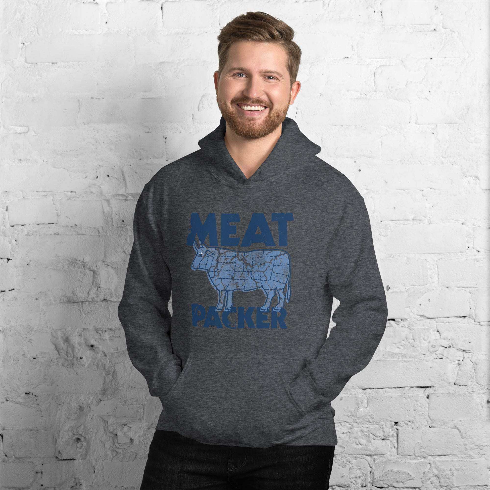 Man wearing grey Meat Packer Pullover Hoodie with blue graphic and text, standing against white brick wall