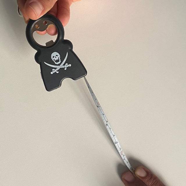 TIM 4-in-1 Keychain with bottle opener, flashlight, tape measure, and skull design being held and measuring length on a white surface