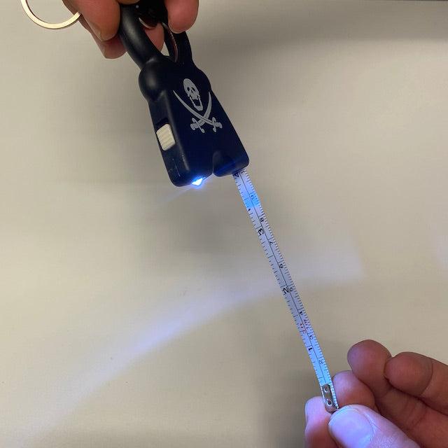 TIM 4-in-1 Keychain with flashlight and measuring tape extended, featuring a black design with skull and crossbones logo.